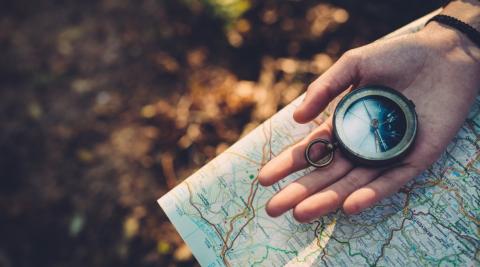 Picture of a hand holding a compass over a map.